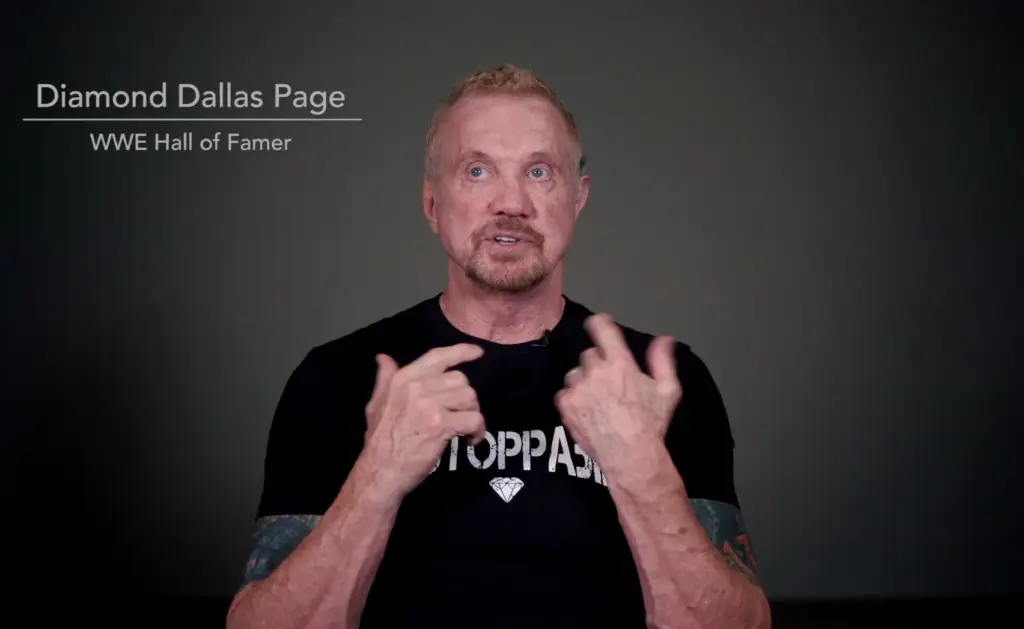 Diamond Dallas Page discussing dental health and implant options, wearing a black shirt with "STOPPA" text, emphasizing the importance of choosing the right dental solutions.